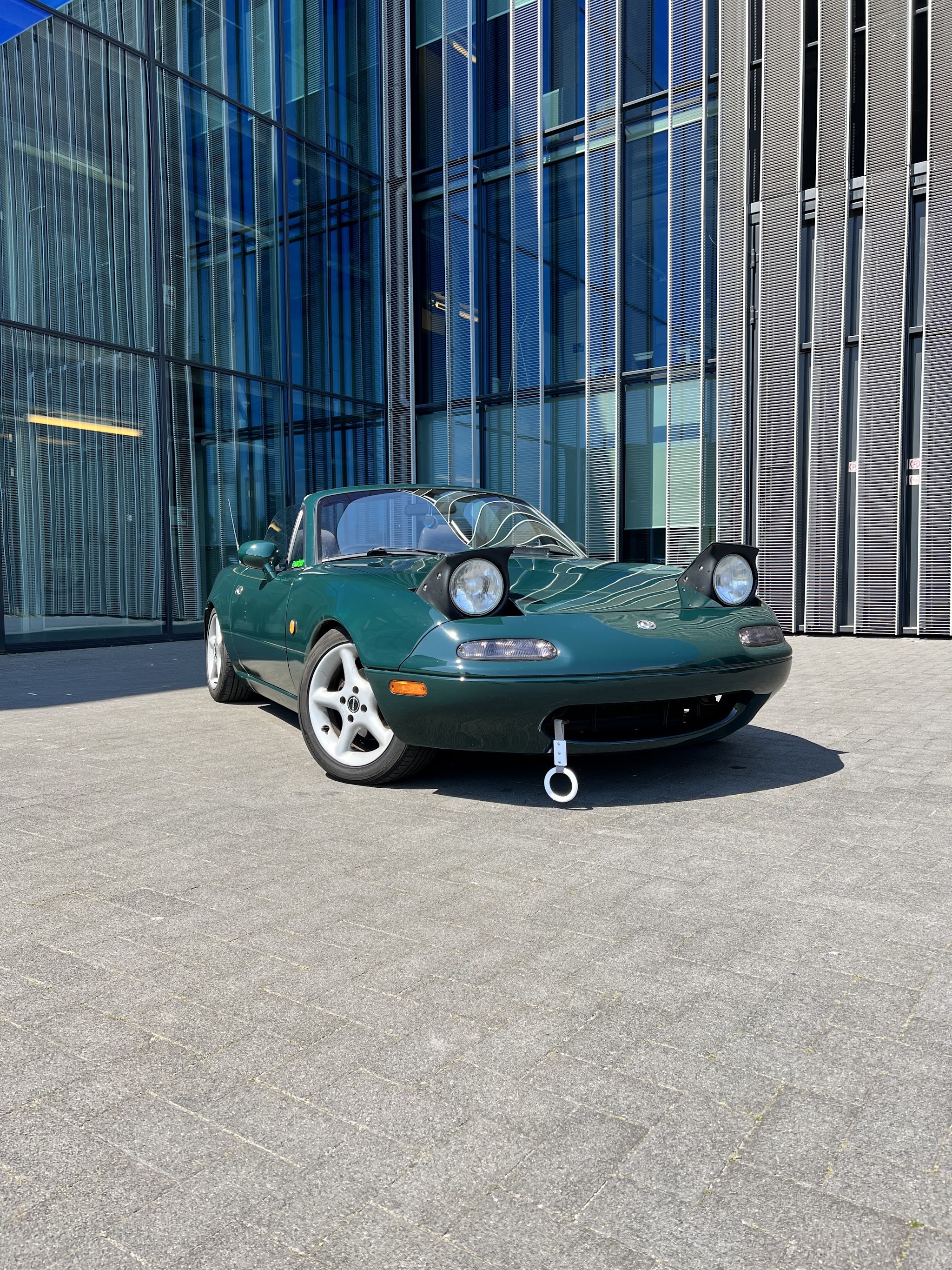Groene Mazda MX-5 cabrio voor een glazen gevel